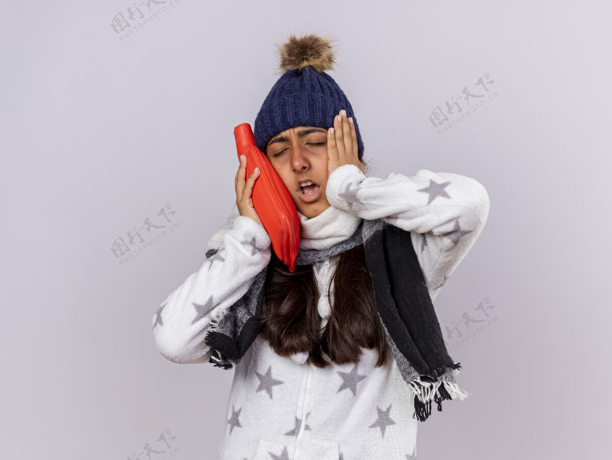 帽子未出嫁的年轻病女孩闭着眼睛戴着带围巾的冬季帽子把热袋水放在脸颊上手封闭女孩