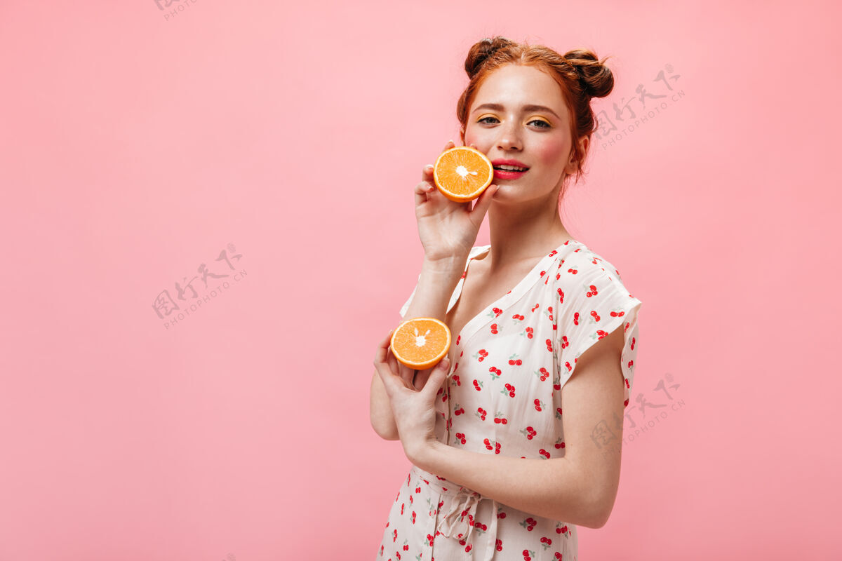 时尚红头发的绿眼睛女人惊奇地盯着镜头 手里拿着粉红色背景上多汁的橘子乐趣时尚快乐