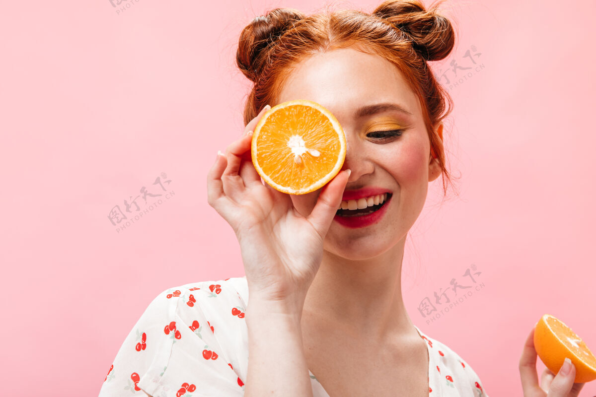 粉色背景年轻精力充沛的红发女子 身穿白色t恤 手拿美味的橘子 背景为粉色年轻头发时尚