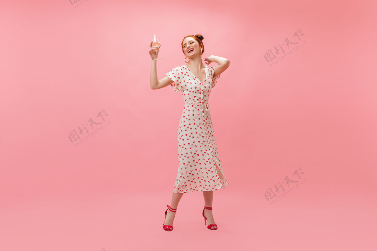 微笑穿着白色樱桃裙的酷女人在粉色背景上吹五彩纸屑乐趣五彩纸屑化妆品