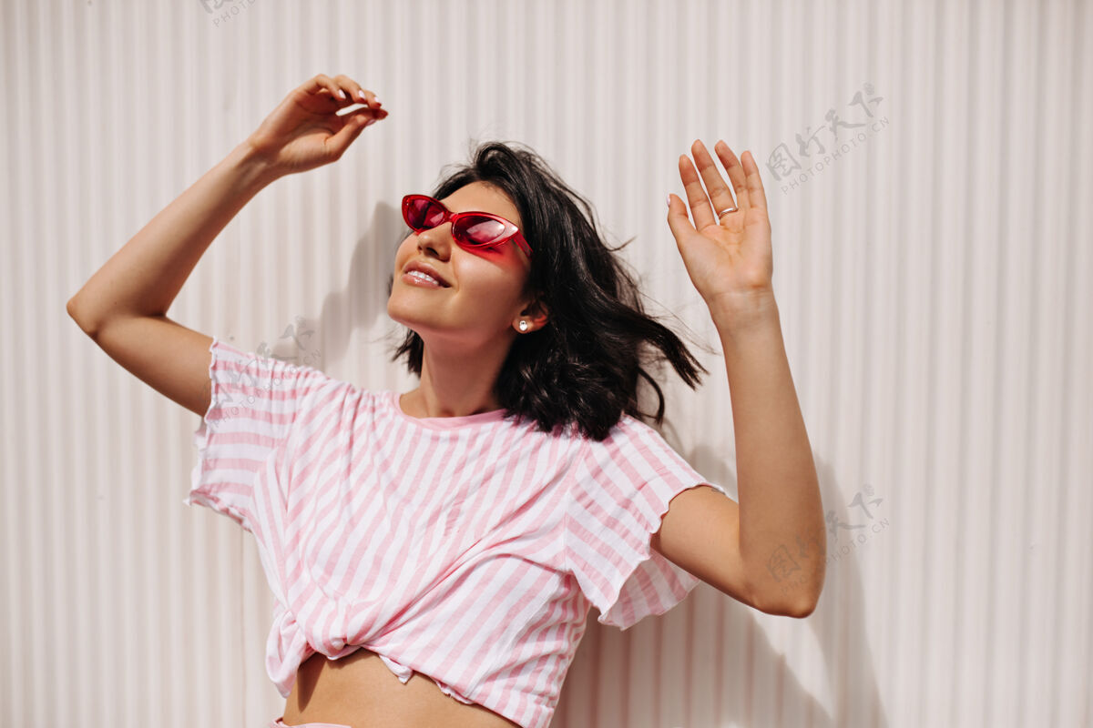 情感快乐的短发女人享受阳光明媚的日子放松的女模特戴着太阳镜站在有纹理的背景上黑发人美丽