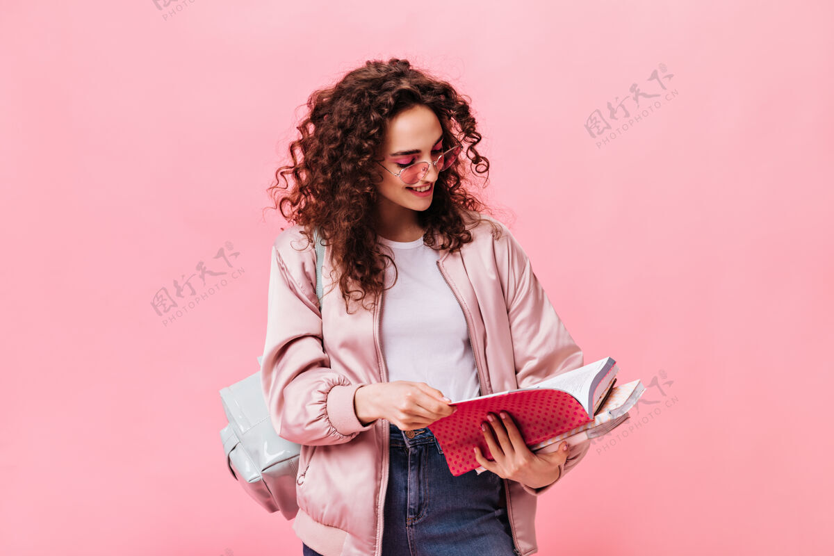 信心穿浅色衣服的女人在粉色背景上读笔记本上的笔记套头衫头发卷发