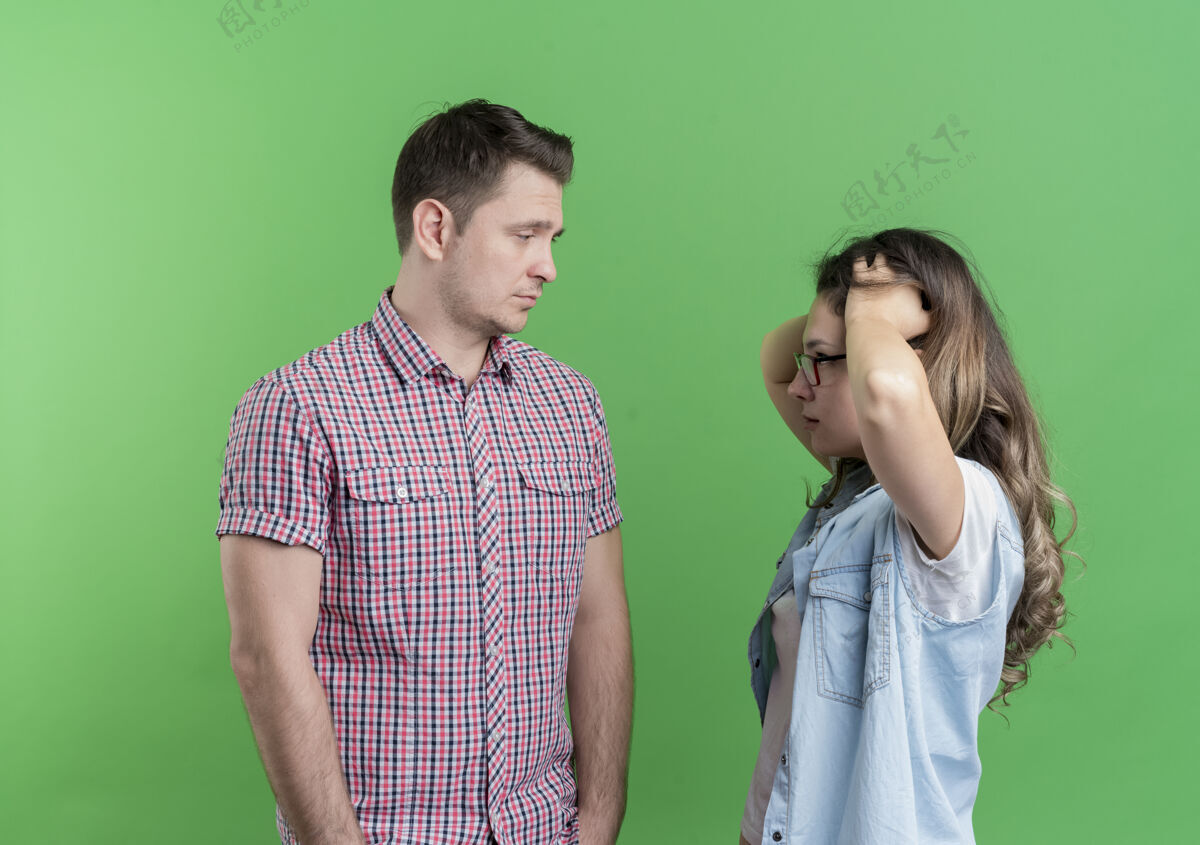 男人一对穿着休闲服的年轻夫妇看着站在绿色墙壁上困惑的女友 满脸愁容的男人不高兴了表情女友不悦