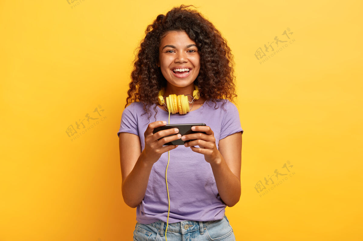 笑在黄色的墙上摆着非洲发型的漂亮年轻女性的头像手机电话人