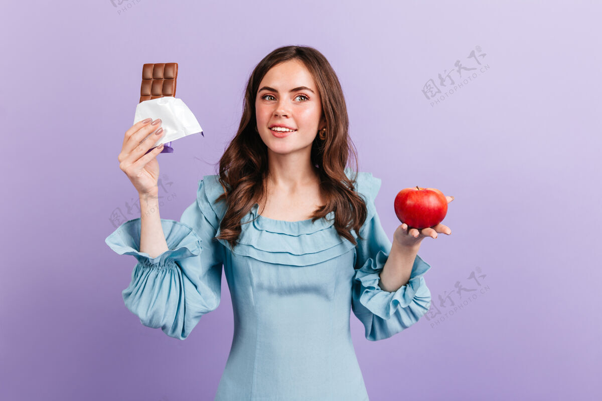 苹果绿眼睛卷曲的黑发女孩在紫色的墙上摆着红苹果和牛奶巧克力黑发可爱成人