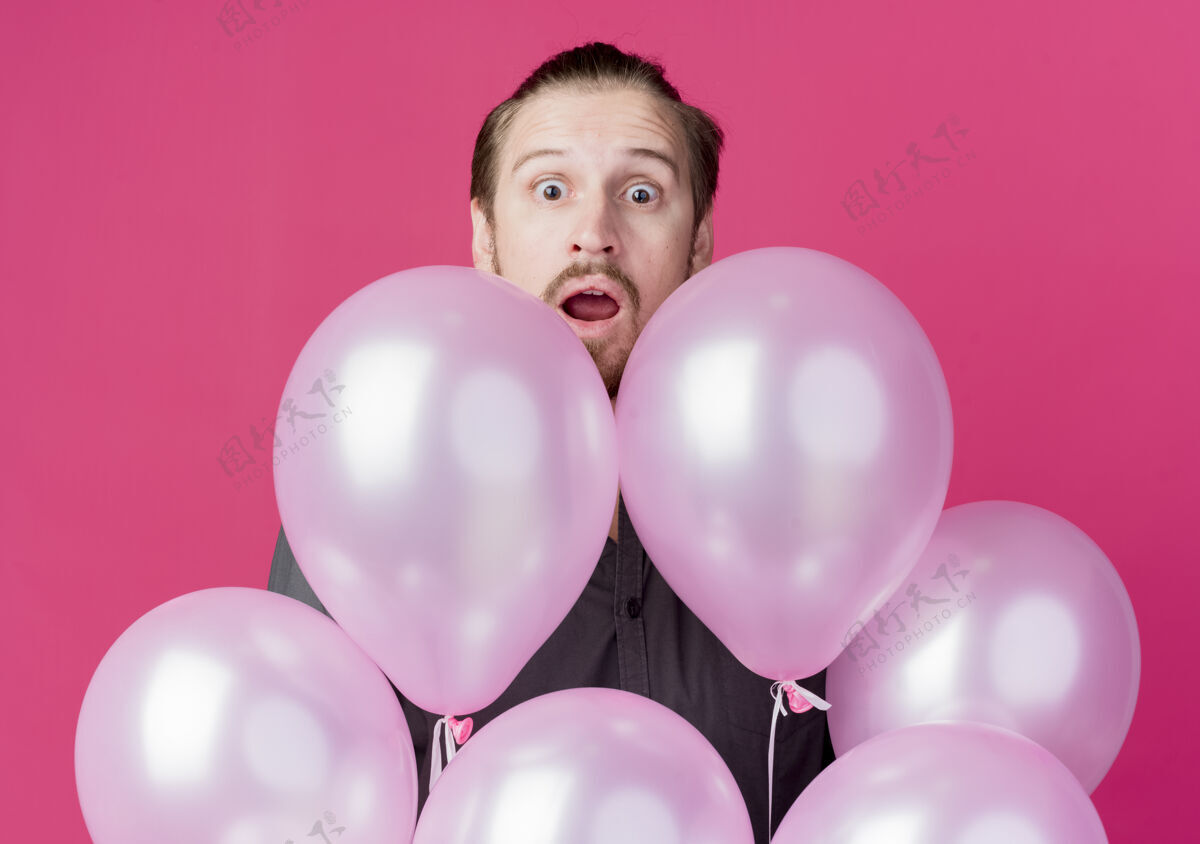 气球庆祝生日聚会的年轻人站在粉红色的墙上 从气球上偷看 既惊讶又惊讶男人偷看惊喜