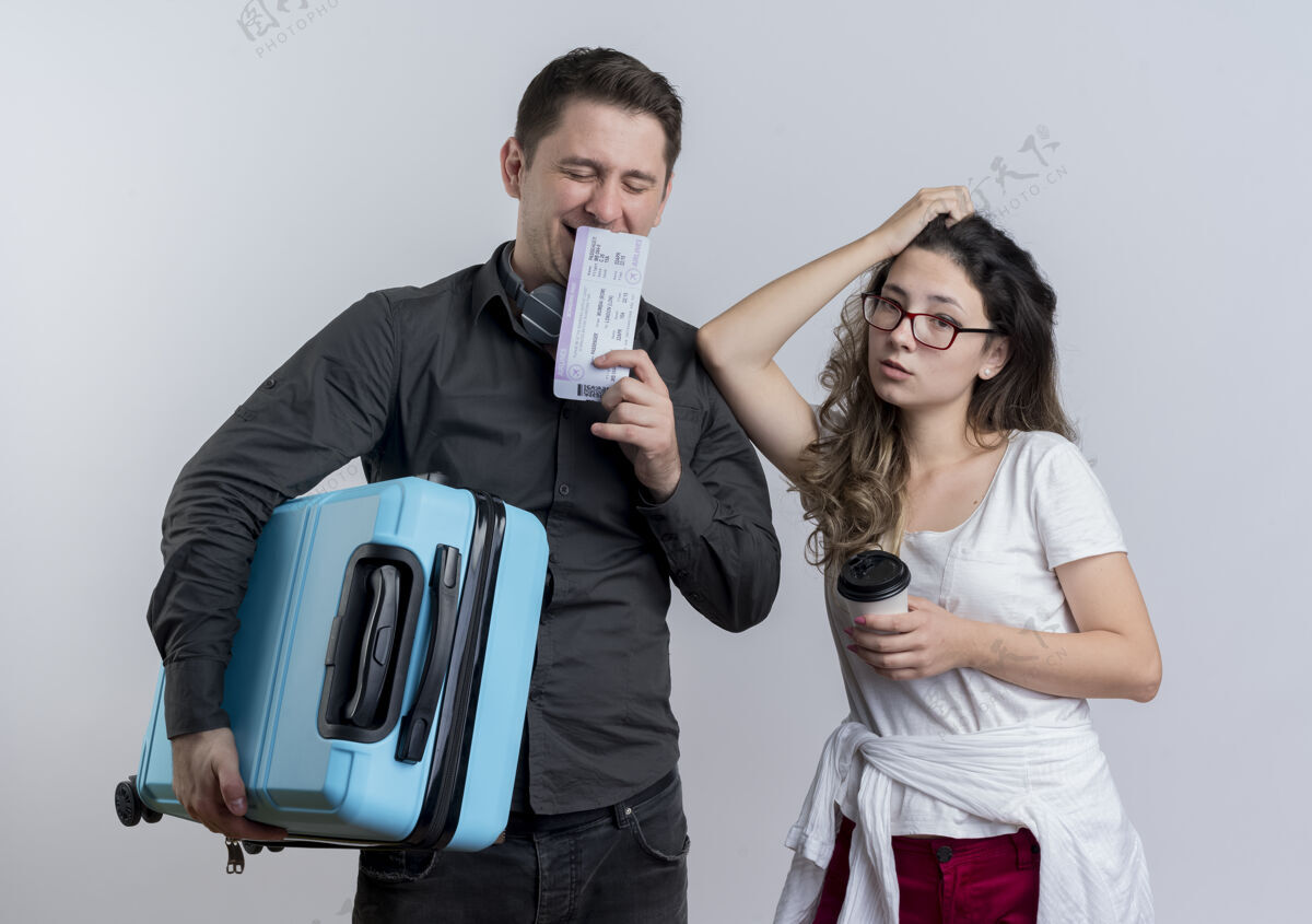 夫妇一对幸福的年轻游客 一男一女拿着手提箱和机票站在白墙上女人男人拿着