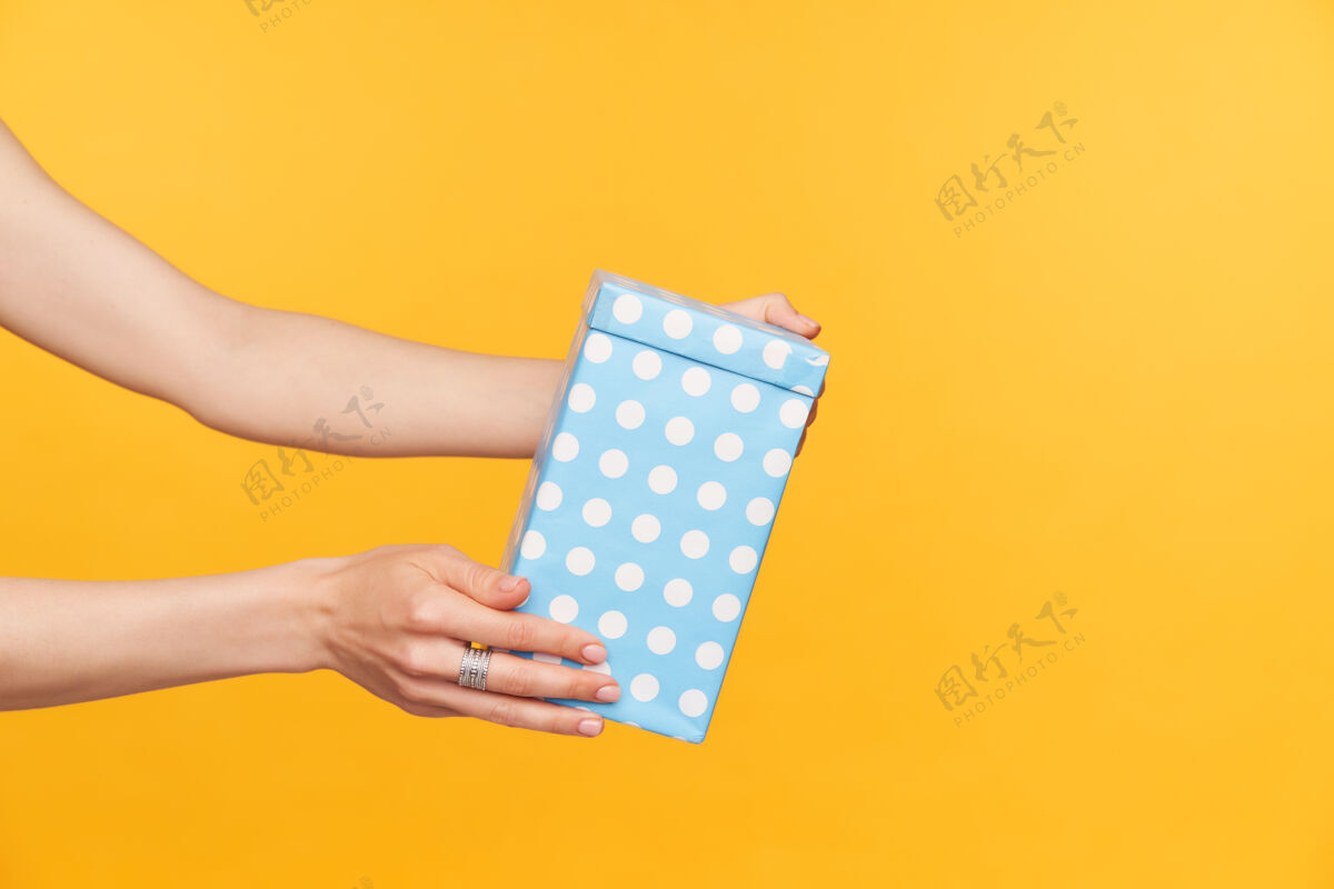 配件摄影棚照片优雅的女性手 皮肤白皙的手被举起 同时举行与礼物盒 去祝贺某人的生日 隔离在黄色背景盒子特写手势