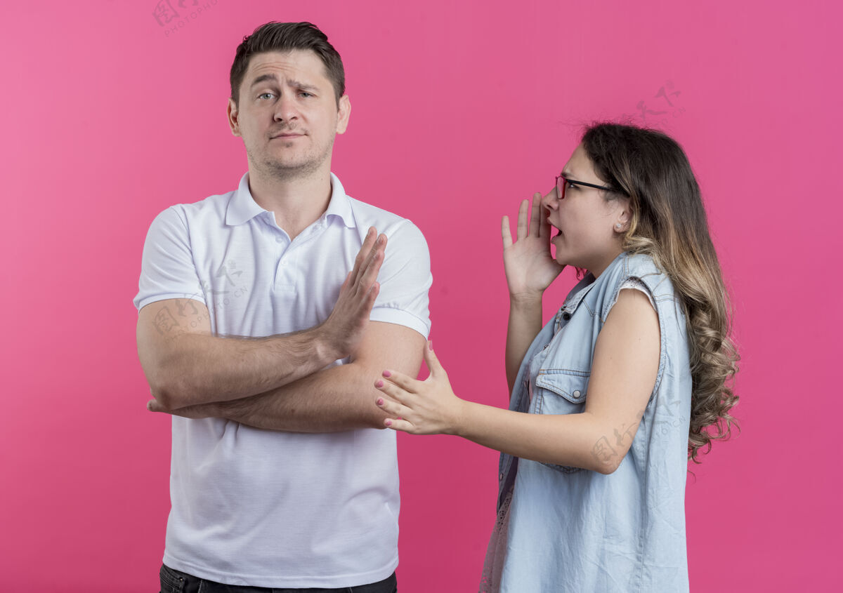 停止一对穿着休闲服的年轻男女不高兴地对她的男朋友大喊大叫 而他站在粉红色的墙上做了个停车的手势男人男朋友情侣