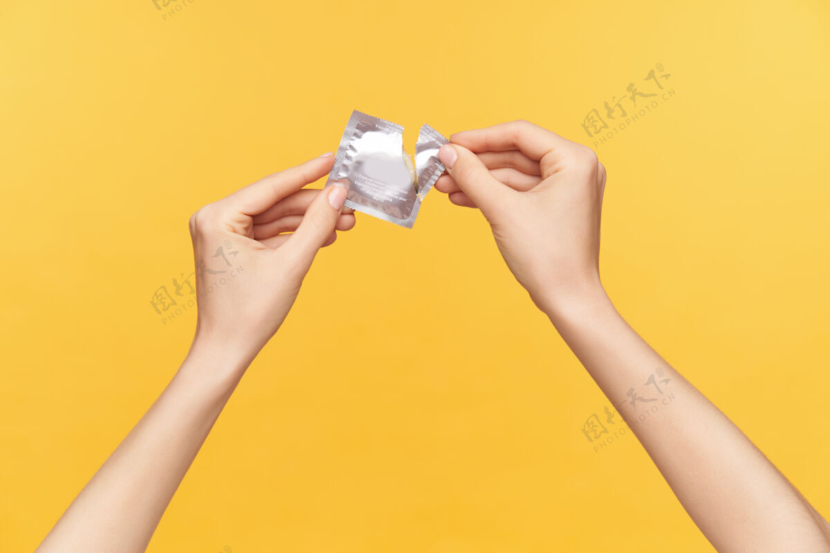 黄色照片中年轻女性举起双手 手上拿着装有避孕套的银包 在橙色背景下被隔离 打开包装关系和性观念手势手指性别