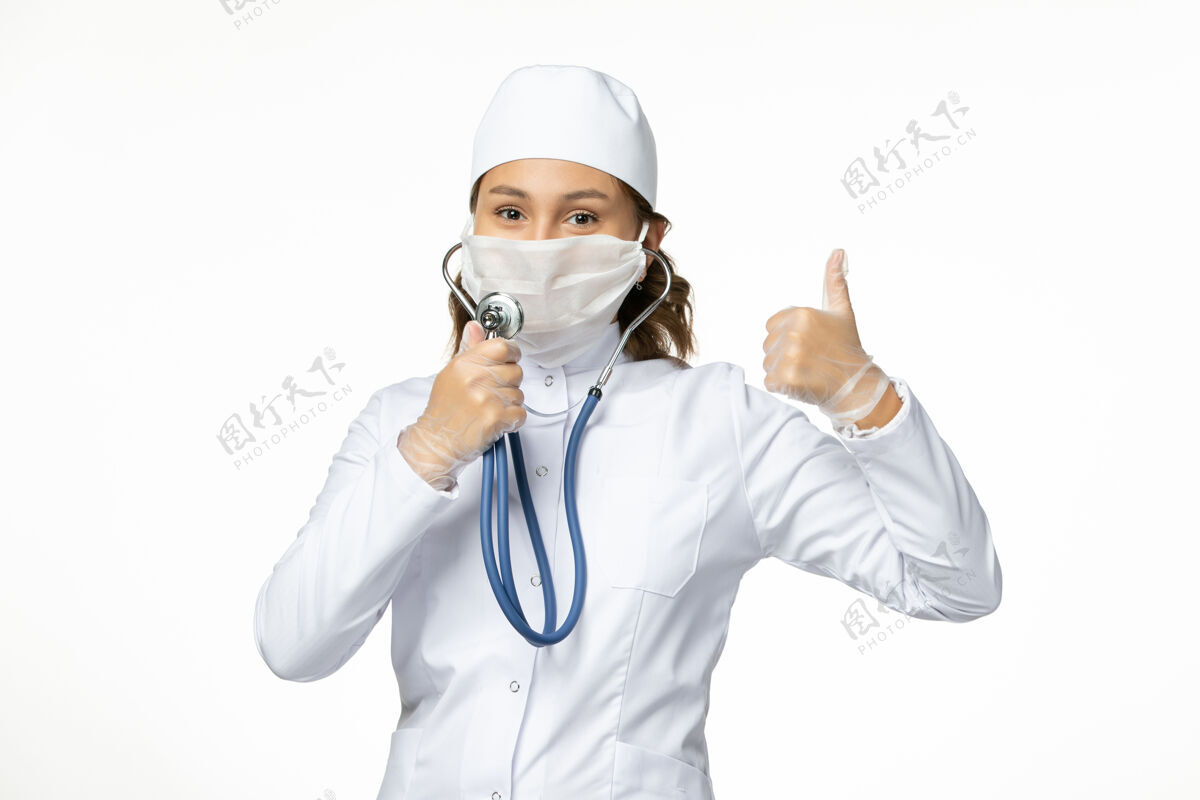 穿戴正面图年轻女医生戴防护无菌口罩因冠状病毒在白色地板上使用听诊器正面病毒听诊器