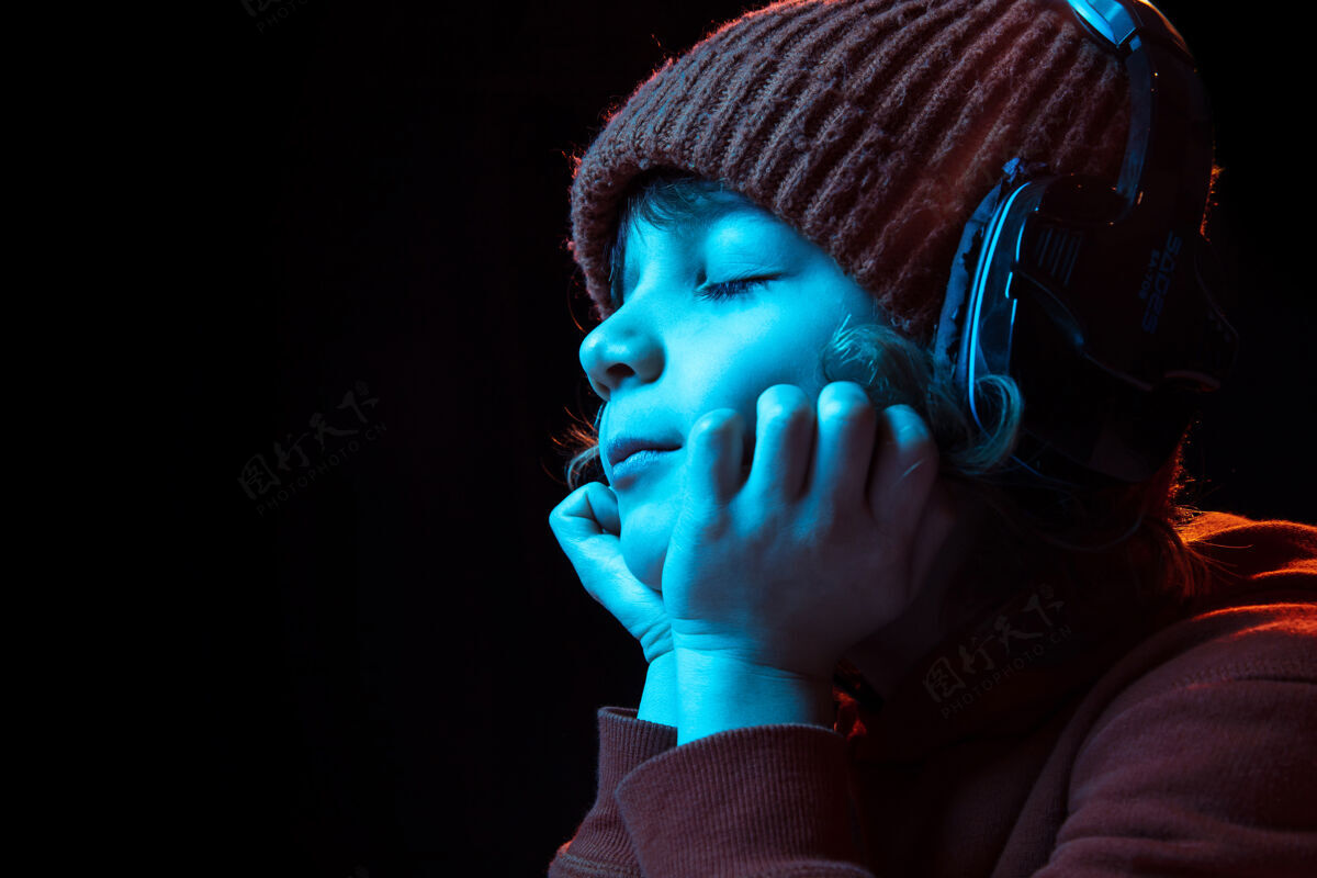 复制空间戴着耳机 闭着眼睛 快乐地听着音乐霓虹灯下深色背景上高加索男孩的画像男性情绪平板电脑