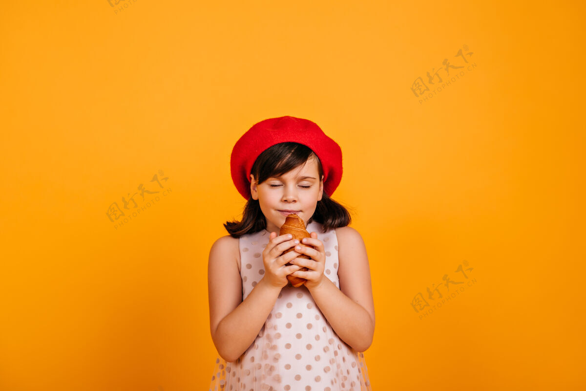 用餐吃羊角面包的可爱饥饿的孩子黑头发的小女孩被隔离在黄色的墙上法国享受女性