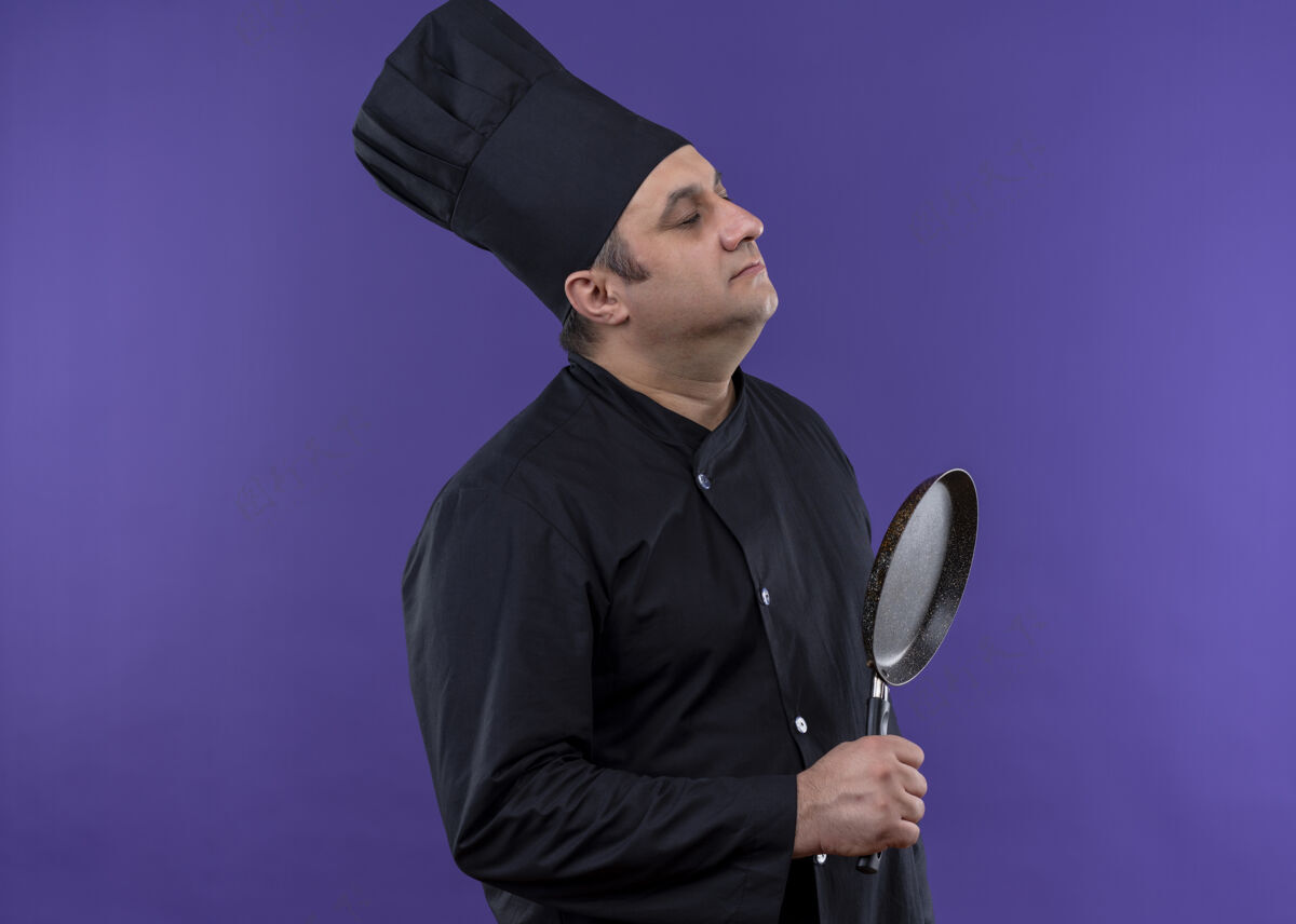 帽子男厨师穿着黑色制服 头戴厨师帽 手里拿着平底锅 站在紫色背景上 心烦意乱紫色厨师黑色