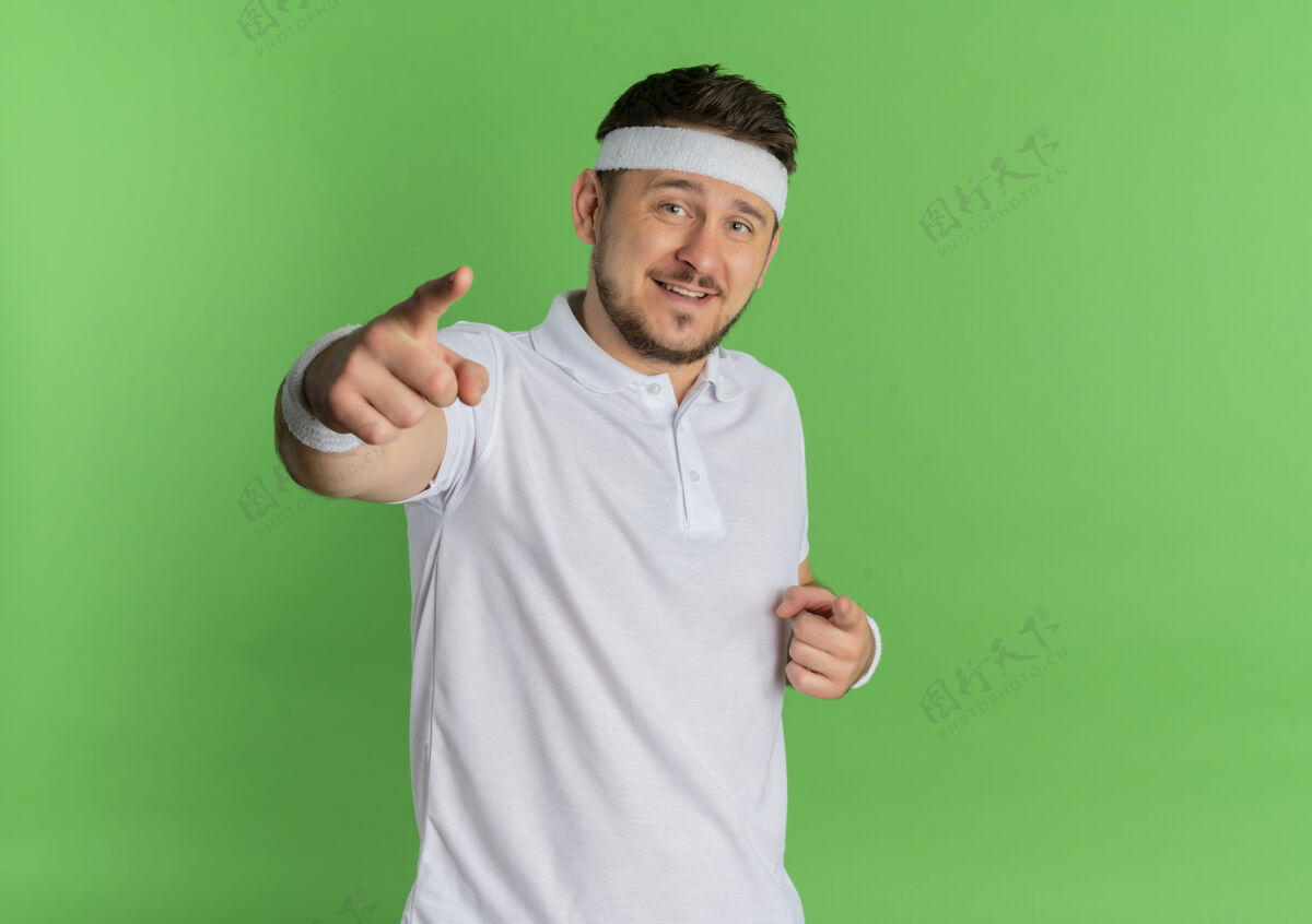 手指身穿白衬衫 头箍 手指对着相机 脸上带着微笑的年轻健身男子站在绿色背景下男人脸手指
