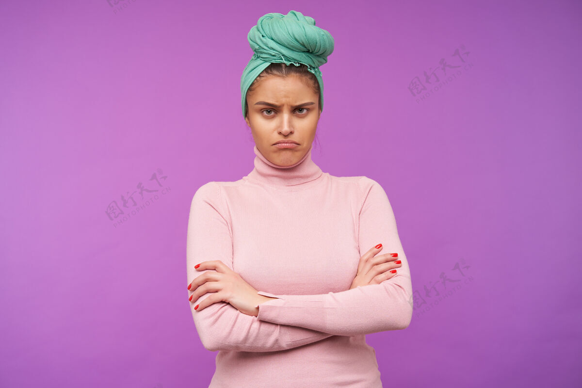 十字架得罪了年轻的棕色头发的女人 自然化妆折叠双手放在胸前 悲伤地看着前面 穿着优雅的紫色墙壁摆姿势自然发型室内