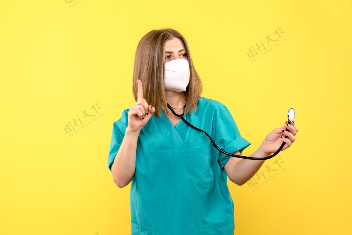 穿着黄色空间上戴面罩的女医生的正面图人人听诊器