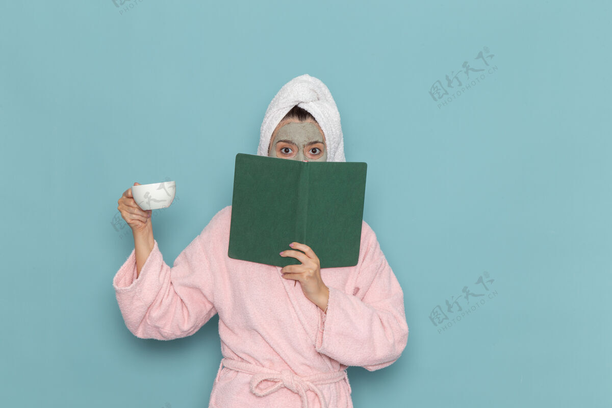 景观正面图穿着粉色浴袍的年轻女性在浅蓝色墙壁上喝咖啡和阅读文案清洁美容自理霜淋浴灯男性前面