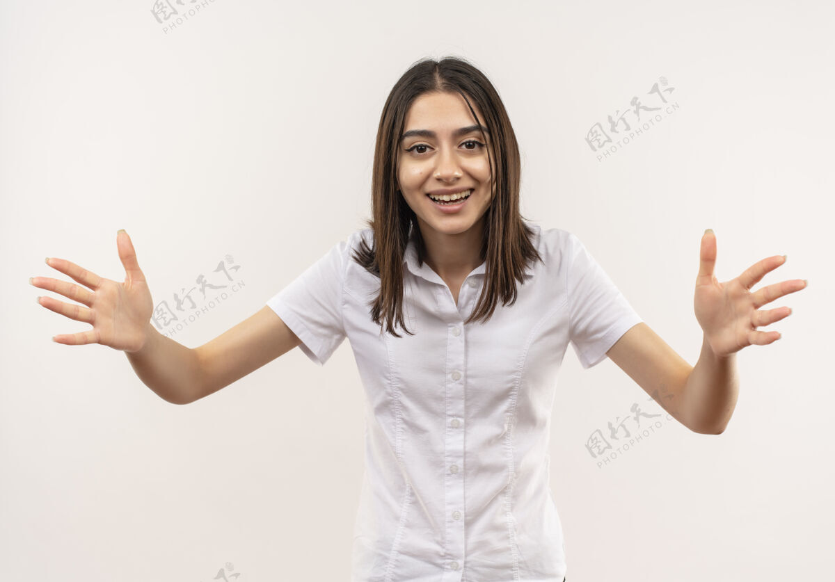 姿势身穿白衬衫的年轻女孩面带微笑 友好地站在白墙上 张开双手 做着欢迎的手势女人人人