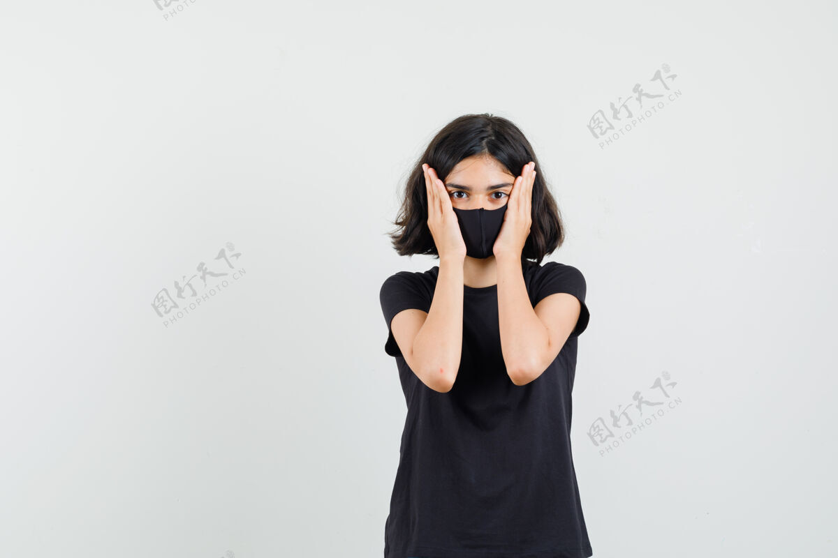 时尚小女孩手拉着脸颊穿着黑色t恤 面具前视图持有可爱美丽