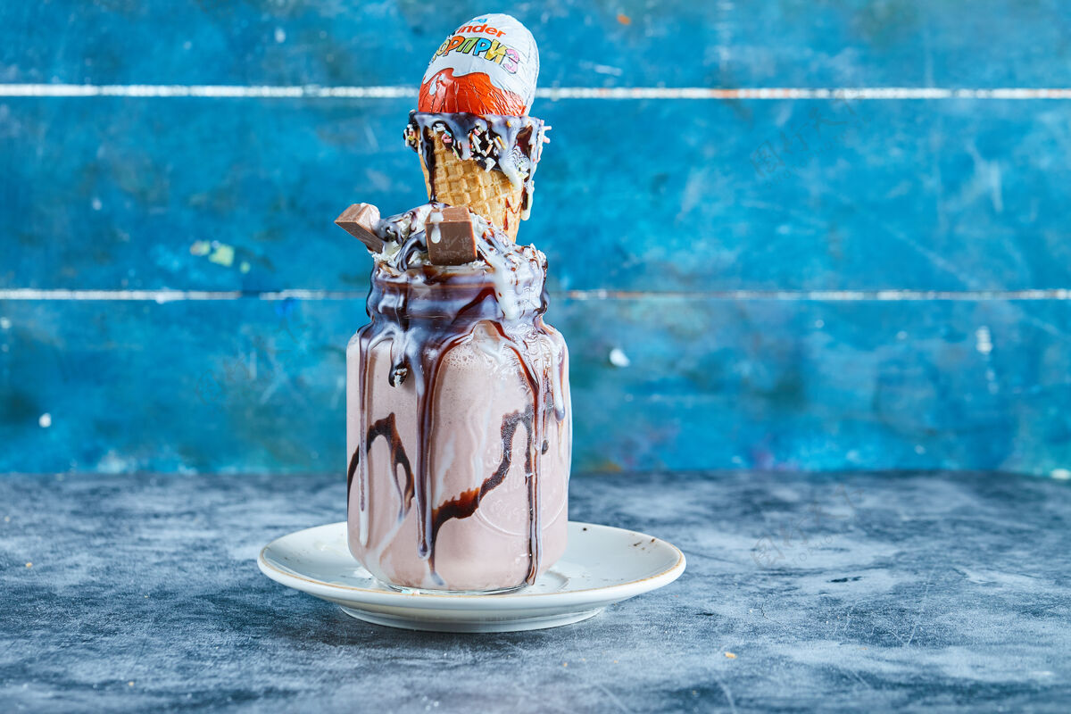 饮料巧克力冰沙和冰淇淋筒 更亲切的惊喜 巧克力糖浆在白色盘子在蓝色的表面盘子马克杯美味