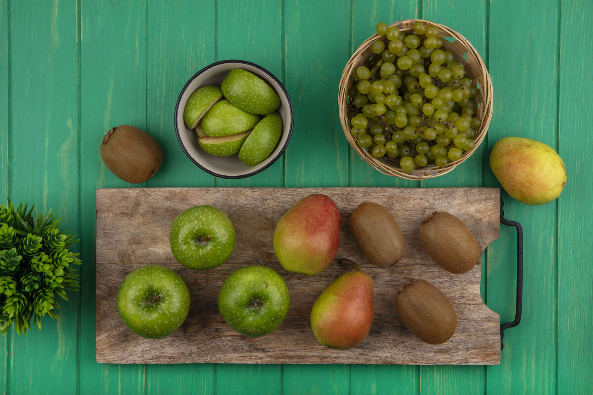 切俯瞰绿色的苹果 砧板上有猕猴桃和梨 绿色的背景上有篮子里的绿色葡萄篮子苹果景观