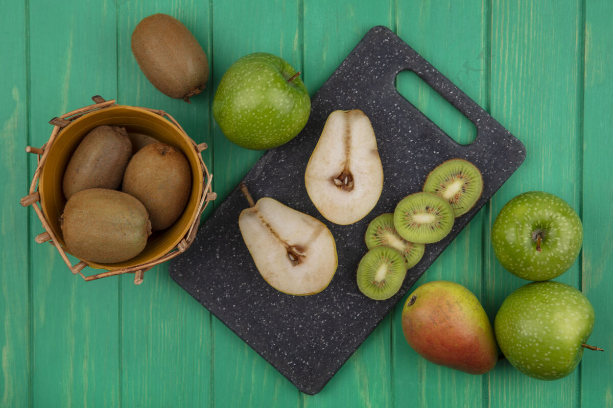 多汁顶视图猕猴桃在一个篮子里 绿色的背景上有一个砧板上的绿色苹果和梨片苹果梨食品