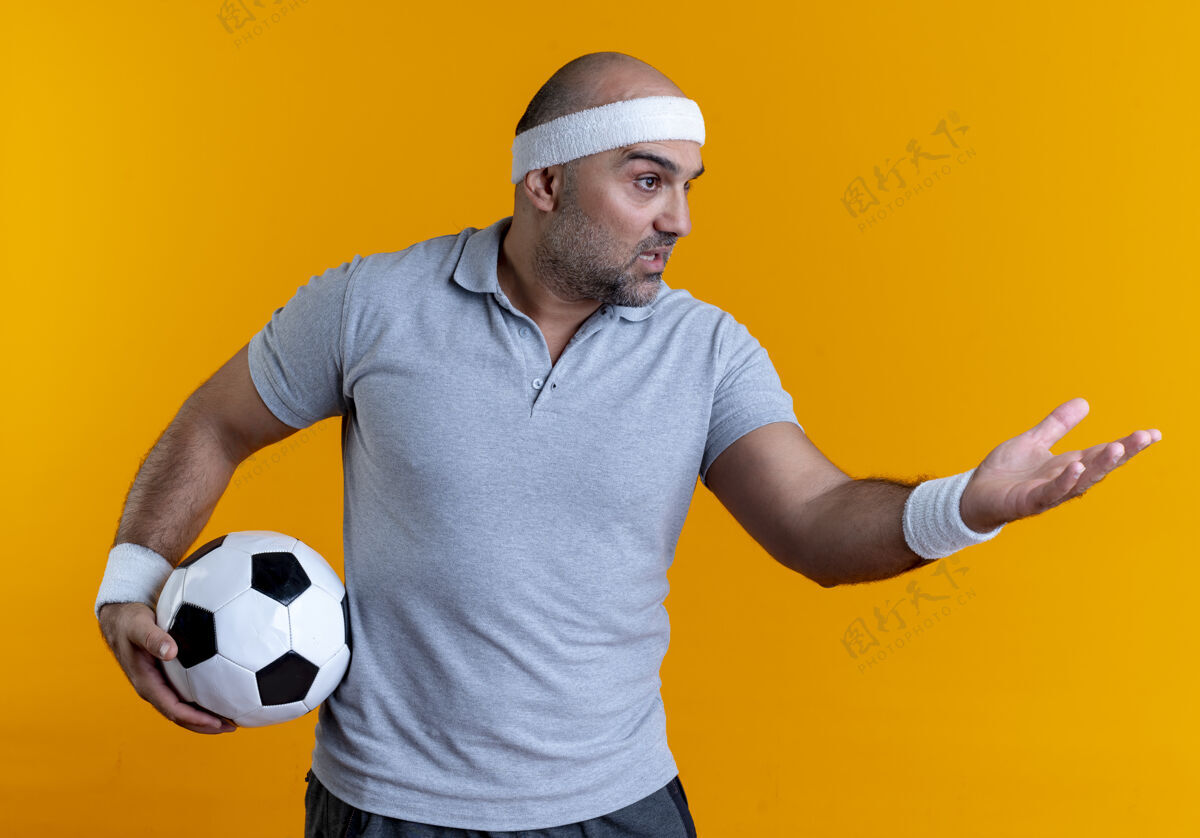 男人成熟的运动型男人戴着头巾 手举足球 站在橘色的墙上一边问或争论男人教练争论