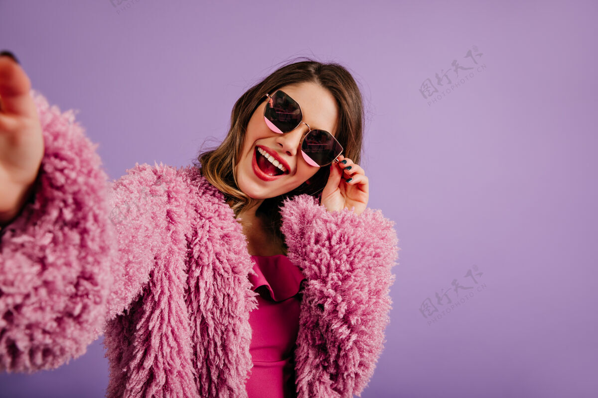女孩戴着墨镜的女人在紫色的墙上摆姿势可爱卷发室内