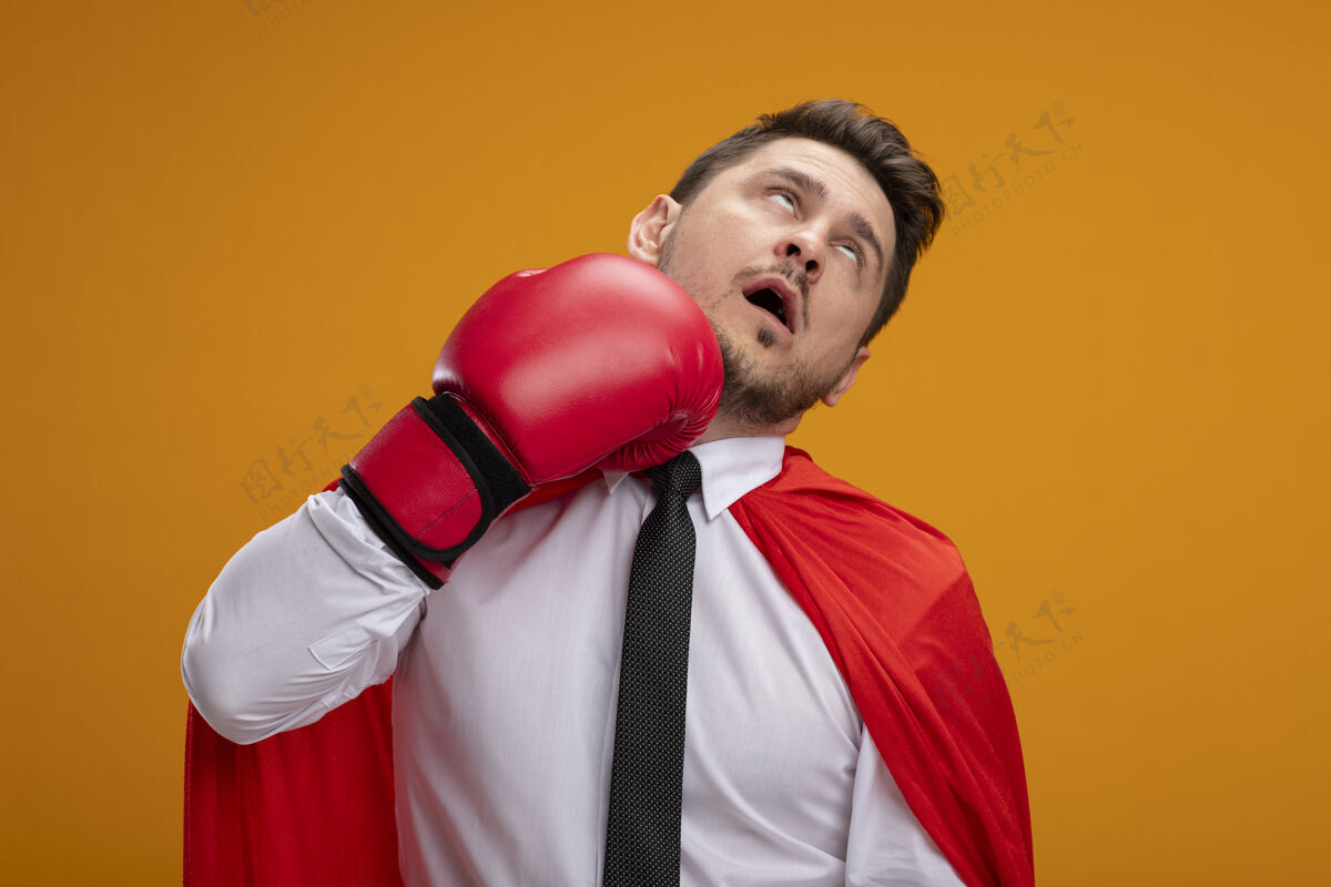 他自己超级英雄商人穿着红色斗篷 戴着拳击手套 站在橘色的墙上打自己站奥兰治拳击