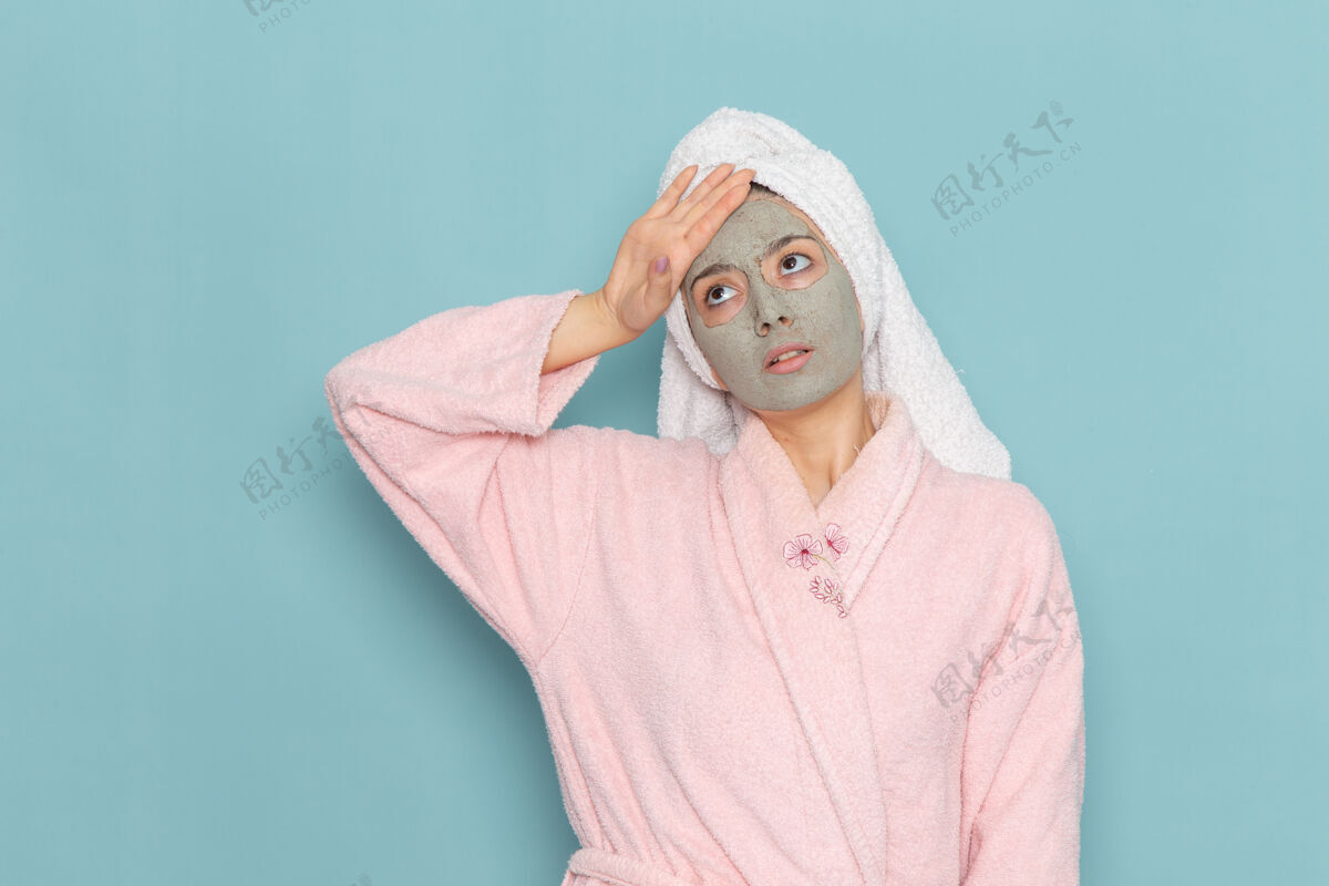 人正面图身着粉色浴袍的年轻女性 忧郁的表情在蓝色墙壁上清洗美容自护霜淋浴自我护理凹陷成人