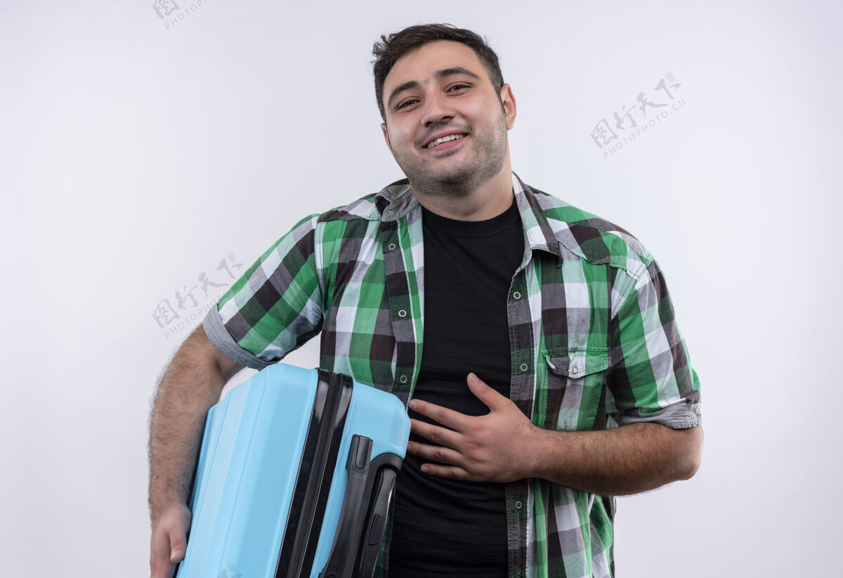人穿着格子衬衫的年轻旅行家手里拿着手提箱 站在白墙上 开心而积极地微笑着微笑站着假期