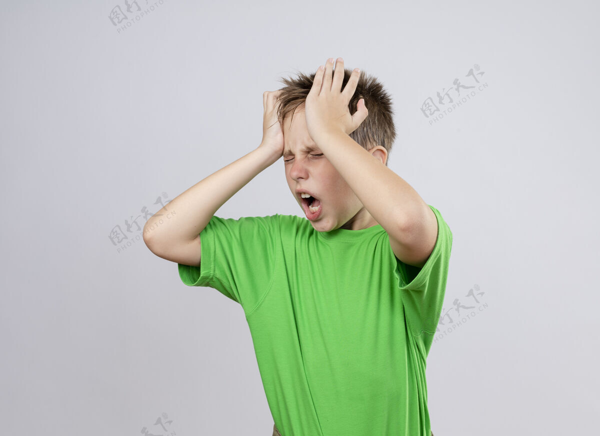 小生病的小男孩穿着绿色t恤 身体不适 头痛得厉害 站在白墙上碰头头男孩强壮