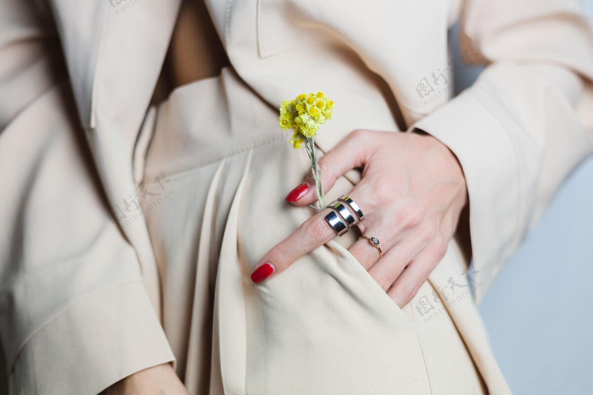 生长近距离拍摄的女人手上的红色指甲两环穿着米色西装黄色可爱的干花在口袋里菊花花蕾无忧无虑