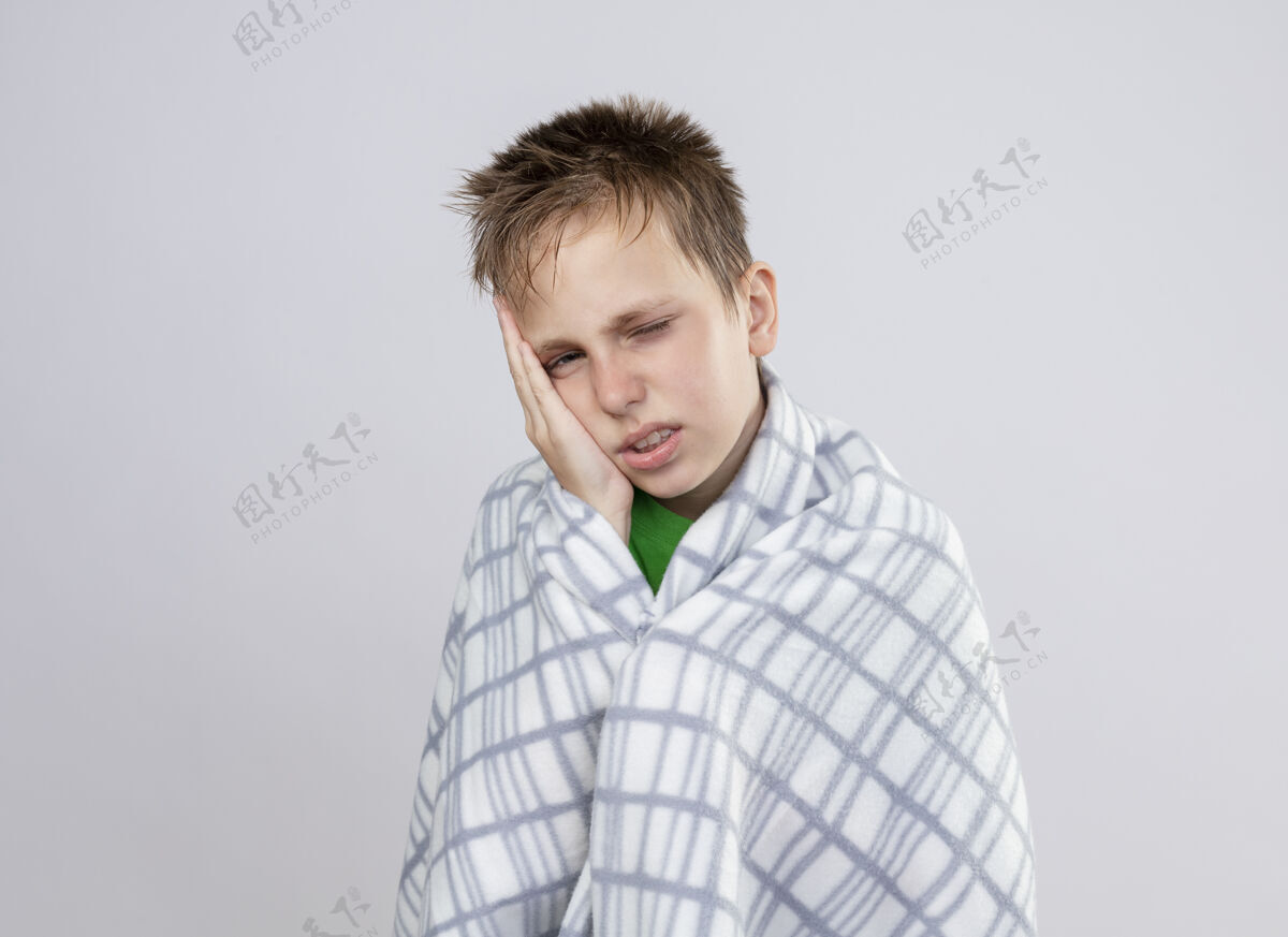 生病生病的小男孩裹着毯子 身体不适 把头靠在手心上 站在白墙上不舒服感觉小站着