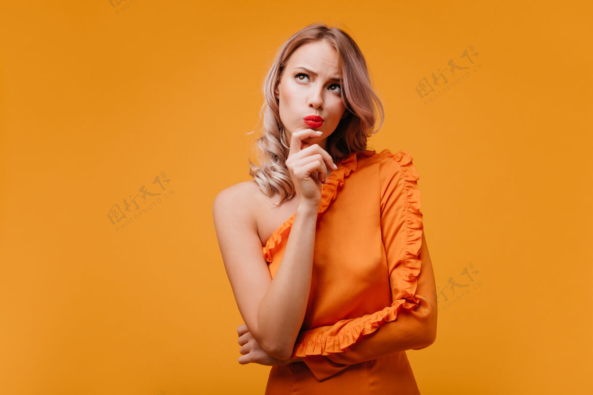 年轻一个穿着橘色裙子的沉思的卷发女人抬起头来欢呼美丽时尚