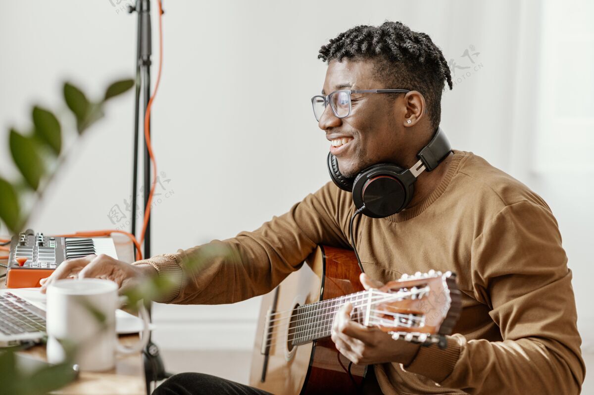 艺术家侧视图笑脸男音乐家在家里弹吉他和笔记本电脑混合电子键盘娱乐创造者
