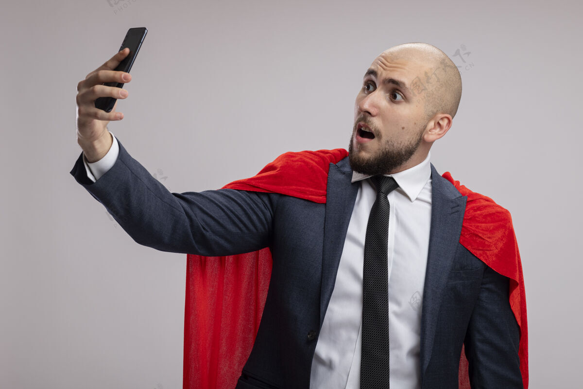 男人超级英雄胡子商人在红斗篷使用智能手机自拍被困惑站在白墙自拍使用超级英雄