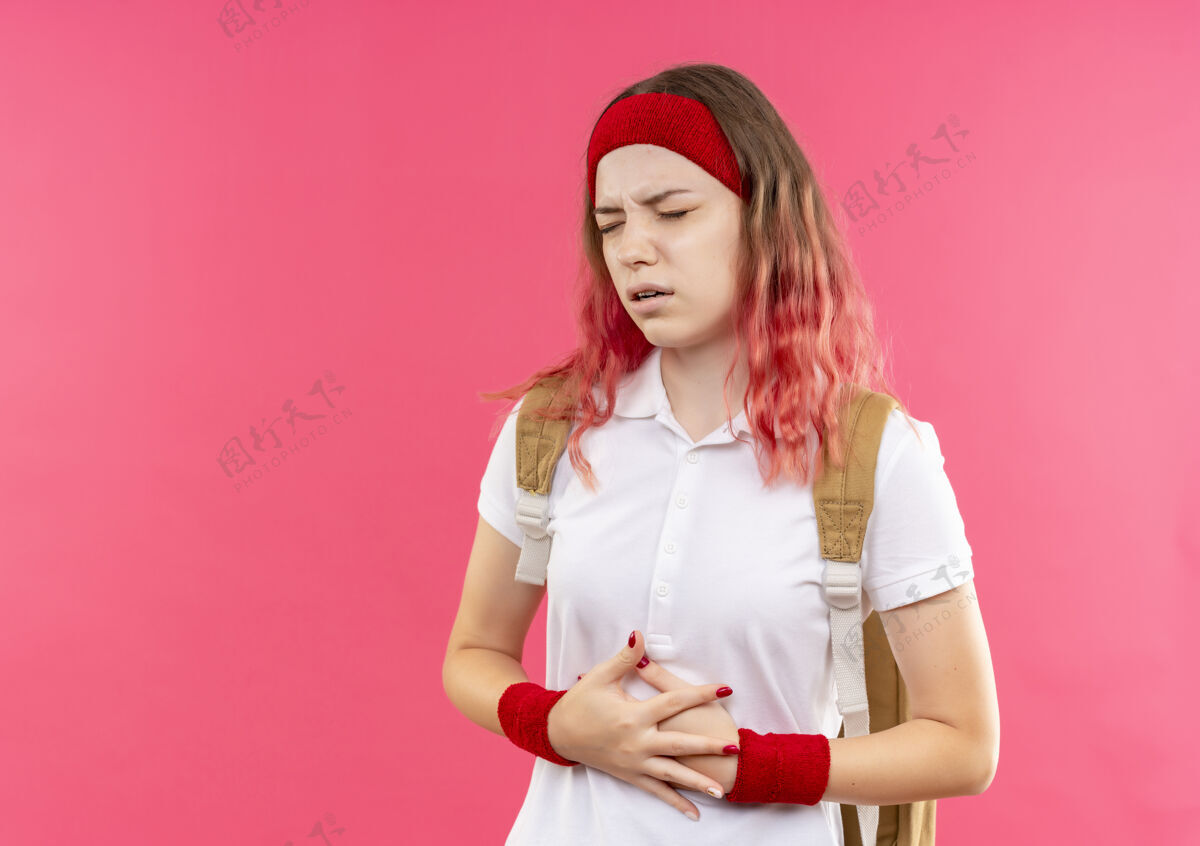 触摸戴着头巾的年轻运动型女人站在粉红色的墙上摸着肚子 看起来不舒服 感觉疼痛运动员感觉女性