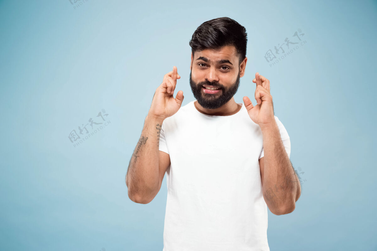 幸运蓝色背景上穿着白衬衫的印度教年轻人的半身特写肖像人类情感 面部表情 广告概念负面空间显示幸运的迹象 微笑事业男性高管