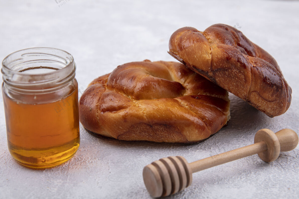 软的侧视图蓬松和柔软的面包与蜂蜜上的玻璃罐和木制蜂蜜勺上的白色背景传统的玻璃中国菜