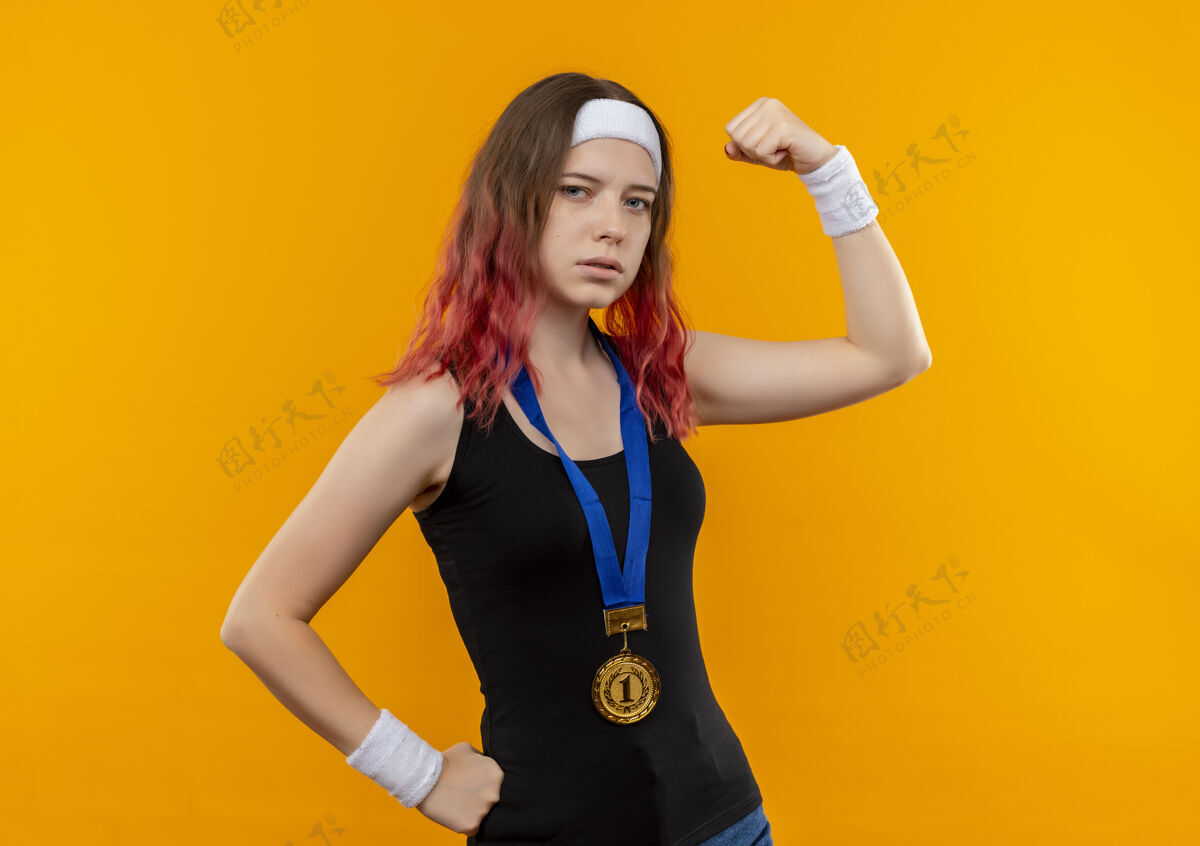 健身身穿运动服 脖子上挂着金牌的年轻健身女士举起拳头 自信地展示着二头肌冠军金牌人物