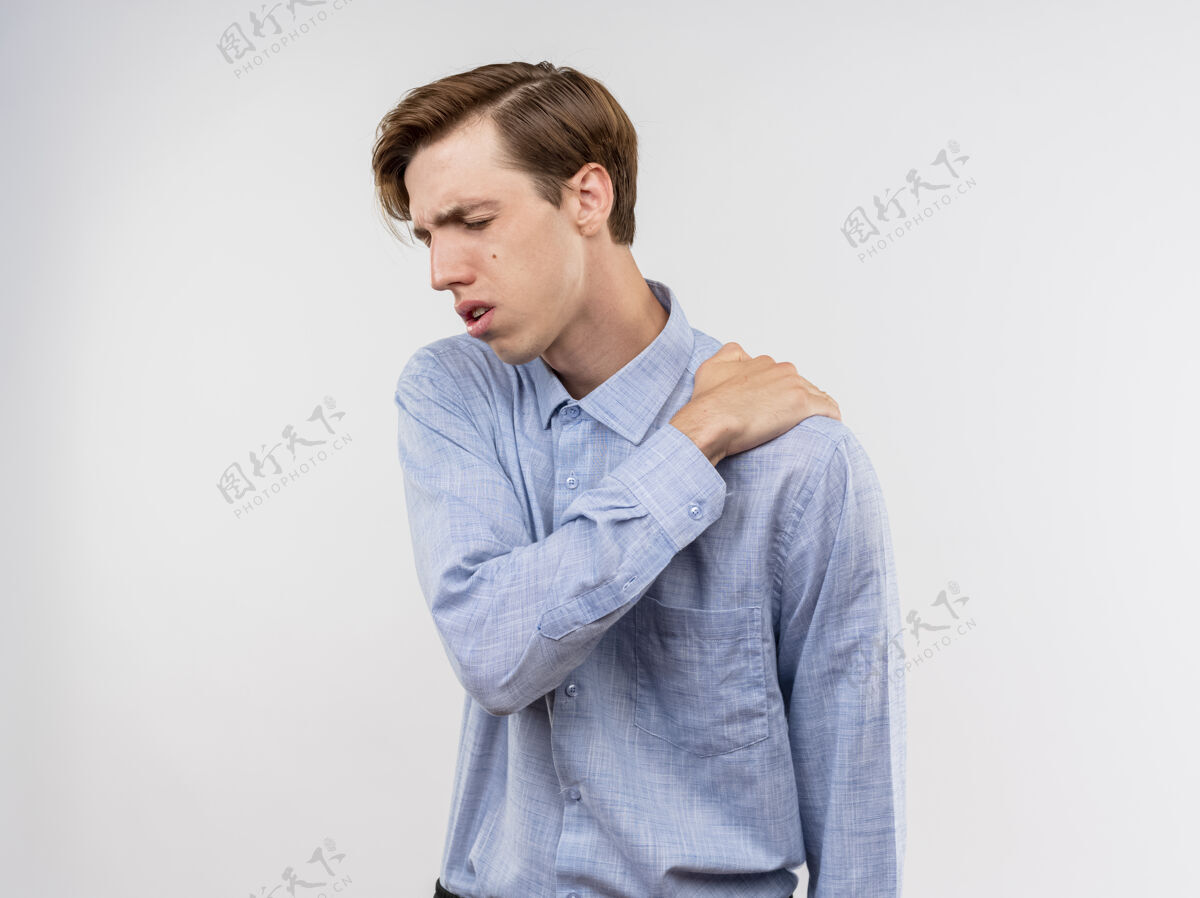 感觉穿着蓝色衬衫的年轻人看起来不舒服 站在白色背景上摸肩膀感到疼痛年轻衬衫疼痛