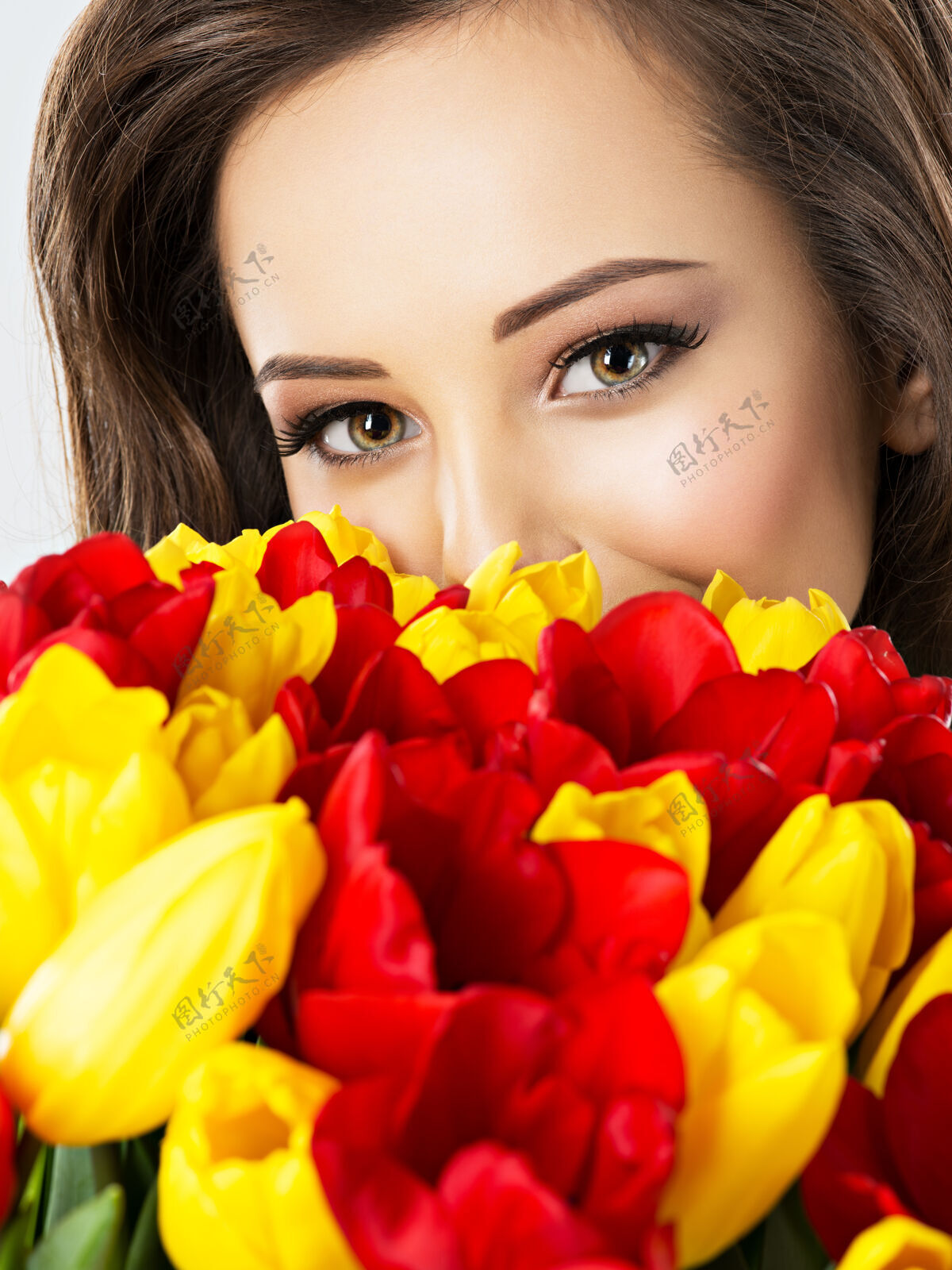 郁金香花丛中美丽女人的眼睛一个漂亮女孩的肖像用红黄色的郁金香遮住脸魅力惊人华丽