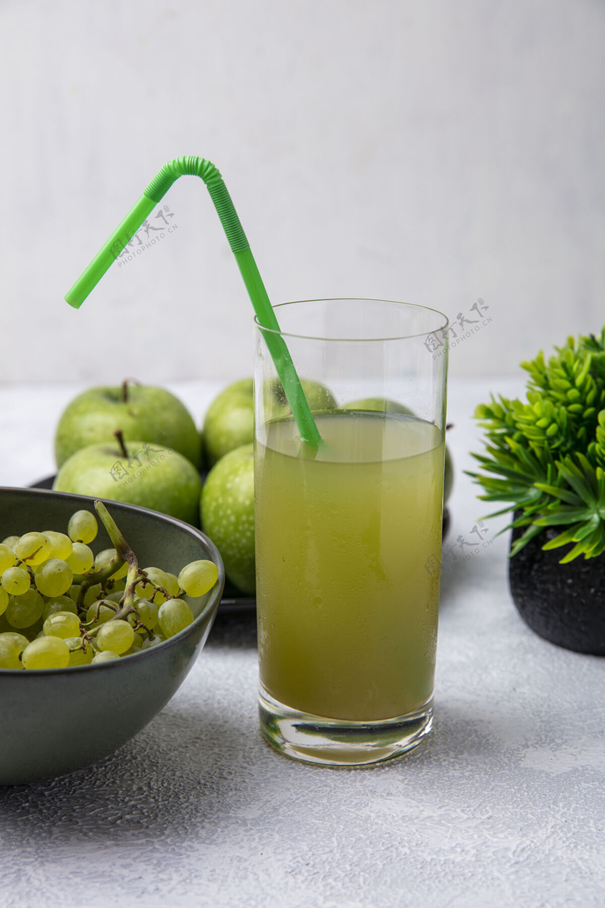 稻草正面视图苹果汁在一个玻璃与绿色吸管绿色葡萄和绿色苹果碗在白色的背景绿色食物果汁