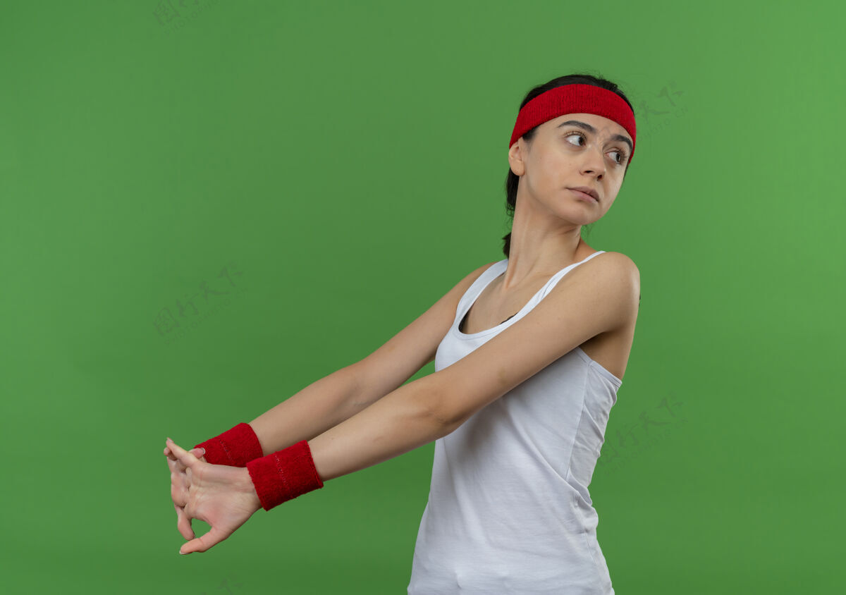女人身穿运动服 头箍舒展的年轻健身女站在绿色的墙壁上 严肃的脸向一边望去运动她自己运动员