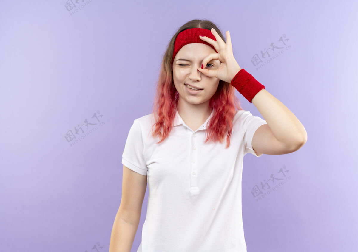 好年轻的运动型女士站在紫色的墙上 用手指看着这个标志 脸上带着微笑女人微笑姿势
