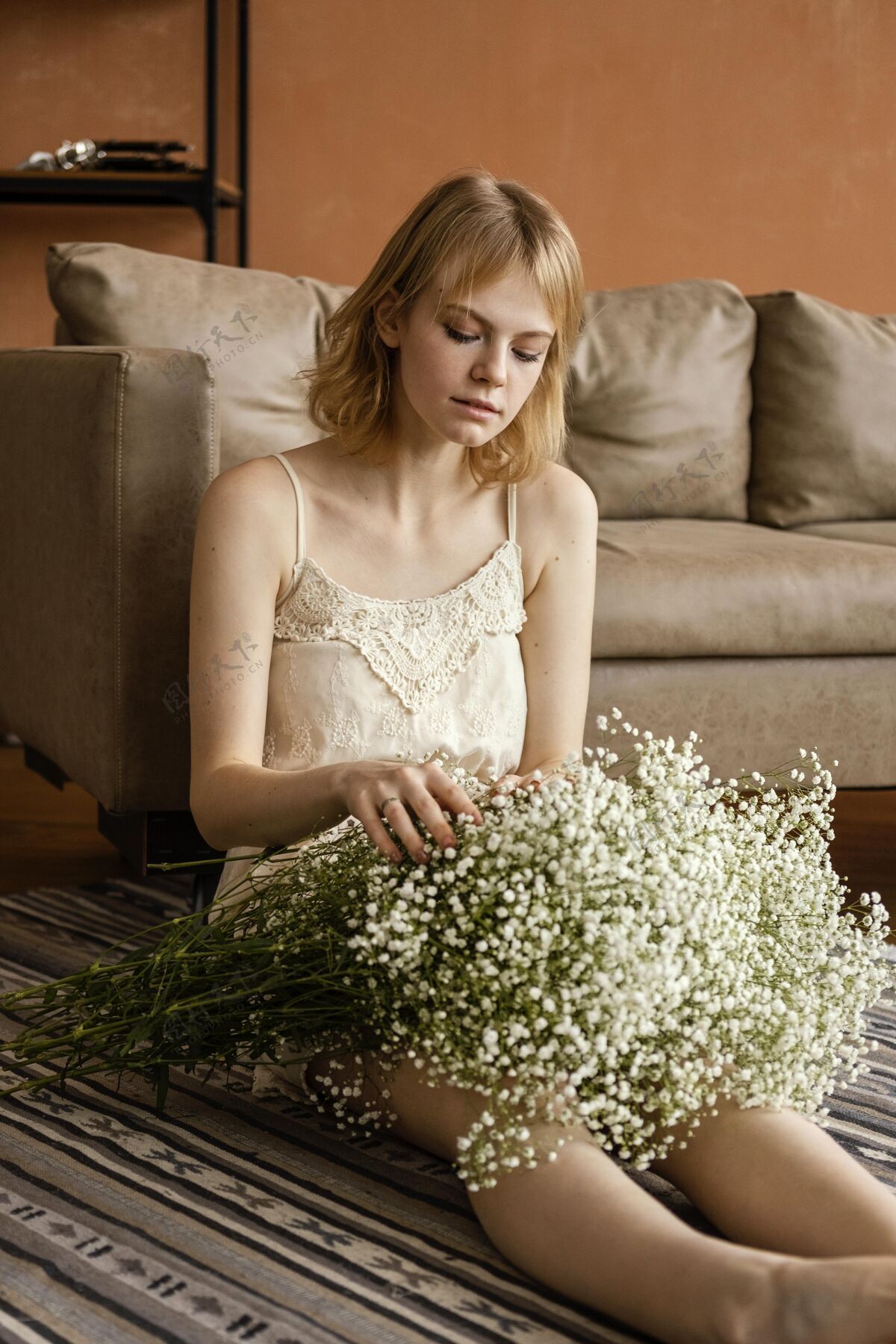 垂直迷人的女人坐在沙发旁 手里捧着一束娇嫩的春花开花春天季节