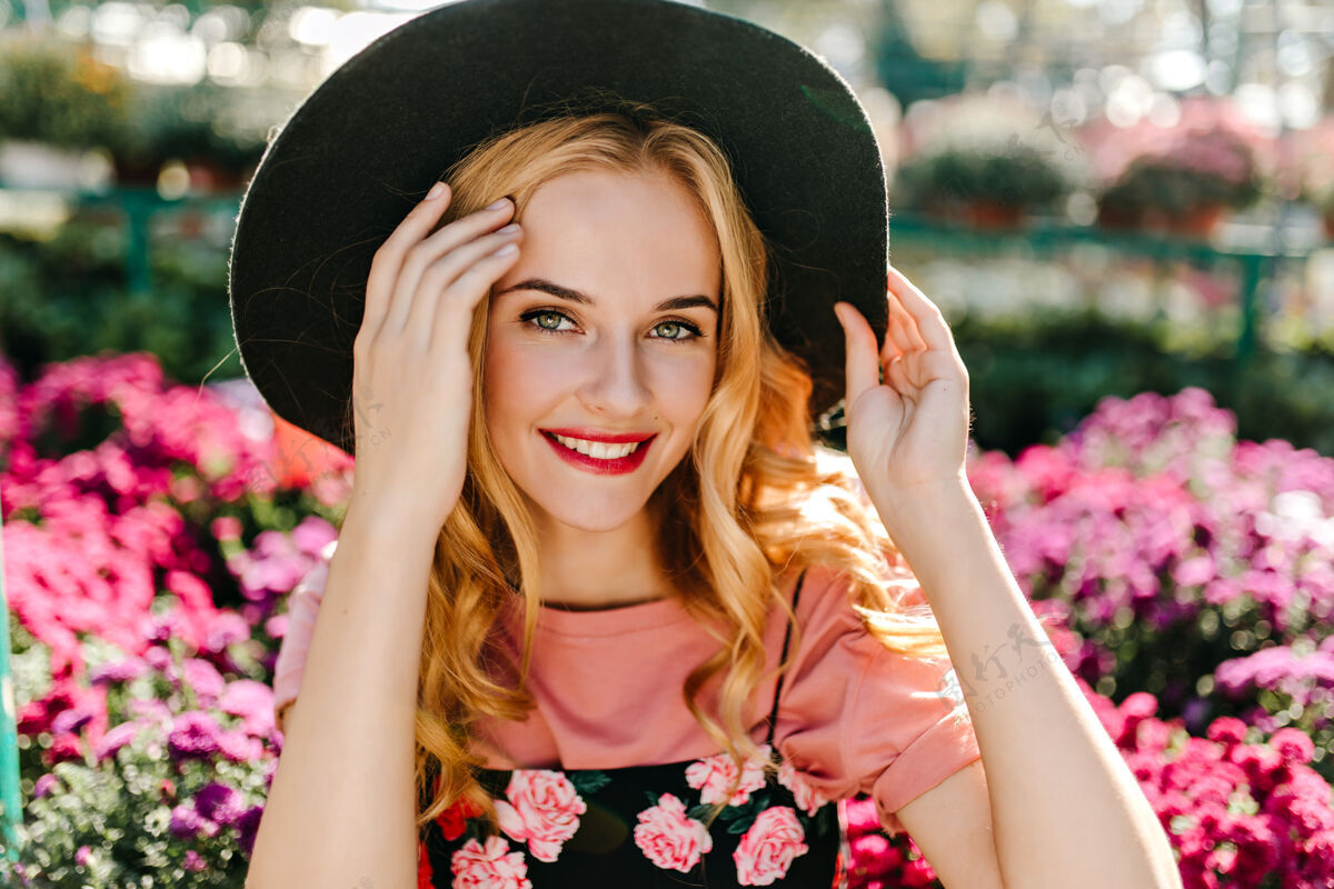 成人一个幽默的大眼睛女人在花园里摆姿势一个戴帽子的快乐女人站在粉红色的花丛里花花园情感