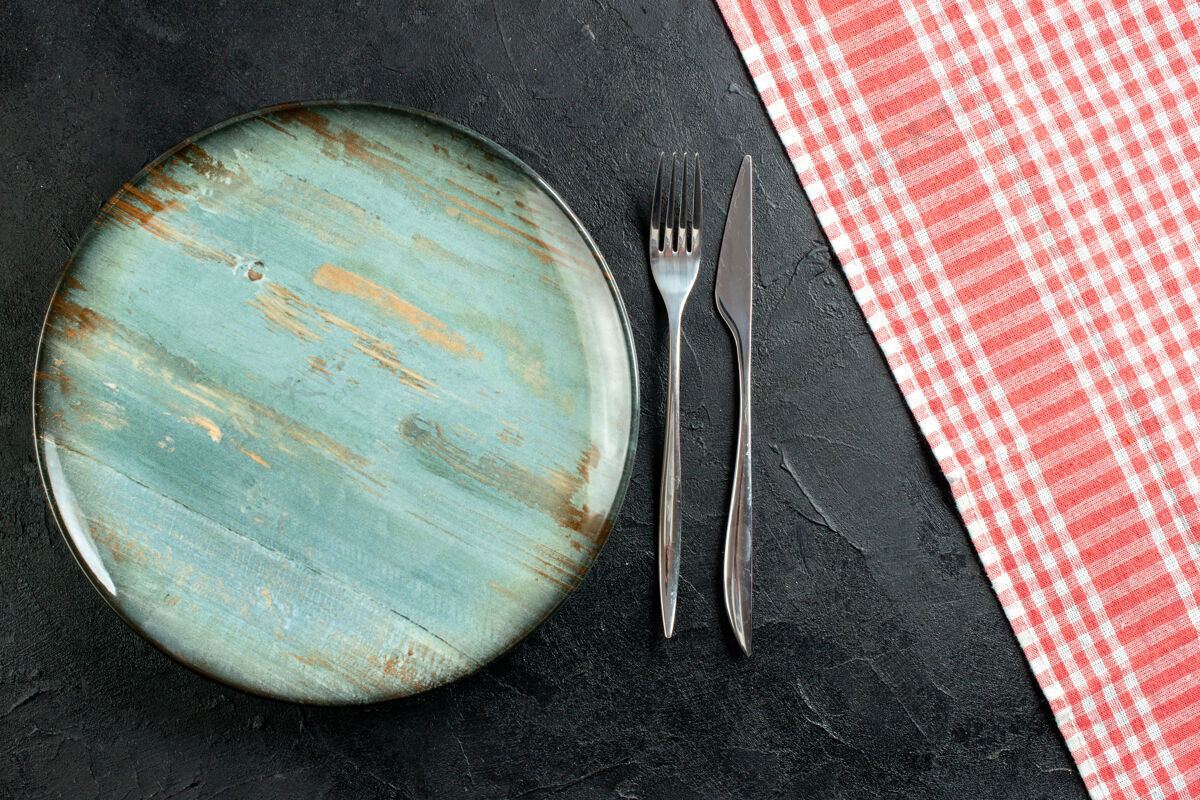 圆盘子顶视图圆形餐叉和餐刀红白格子桌布放在黑桌子上用具刀视图